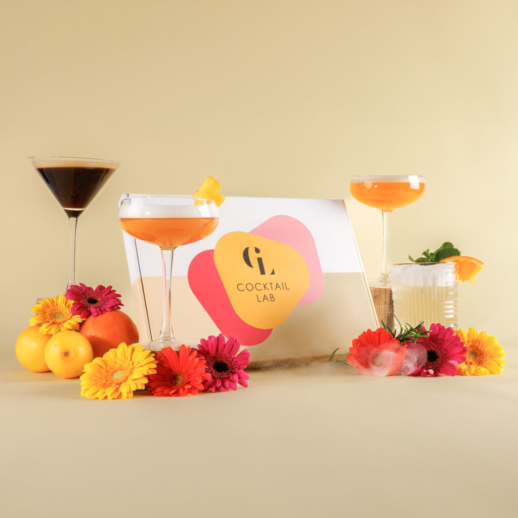 Cocktail Lab box met geserveerde cocktails in verschillende glazen, bloemen en citrus op gele achtergrond – zelf samenstellen box groot